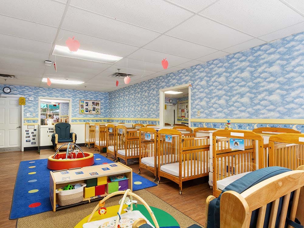 Cribs in a daycare room with play mats and toys