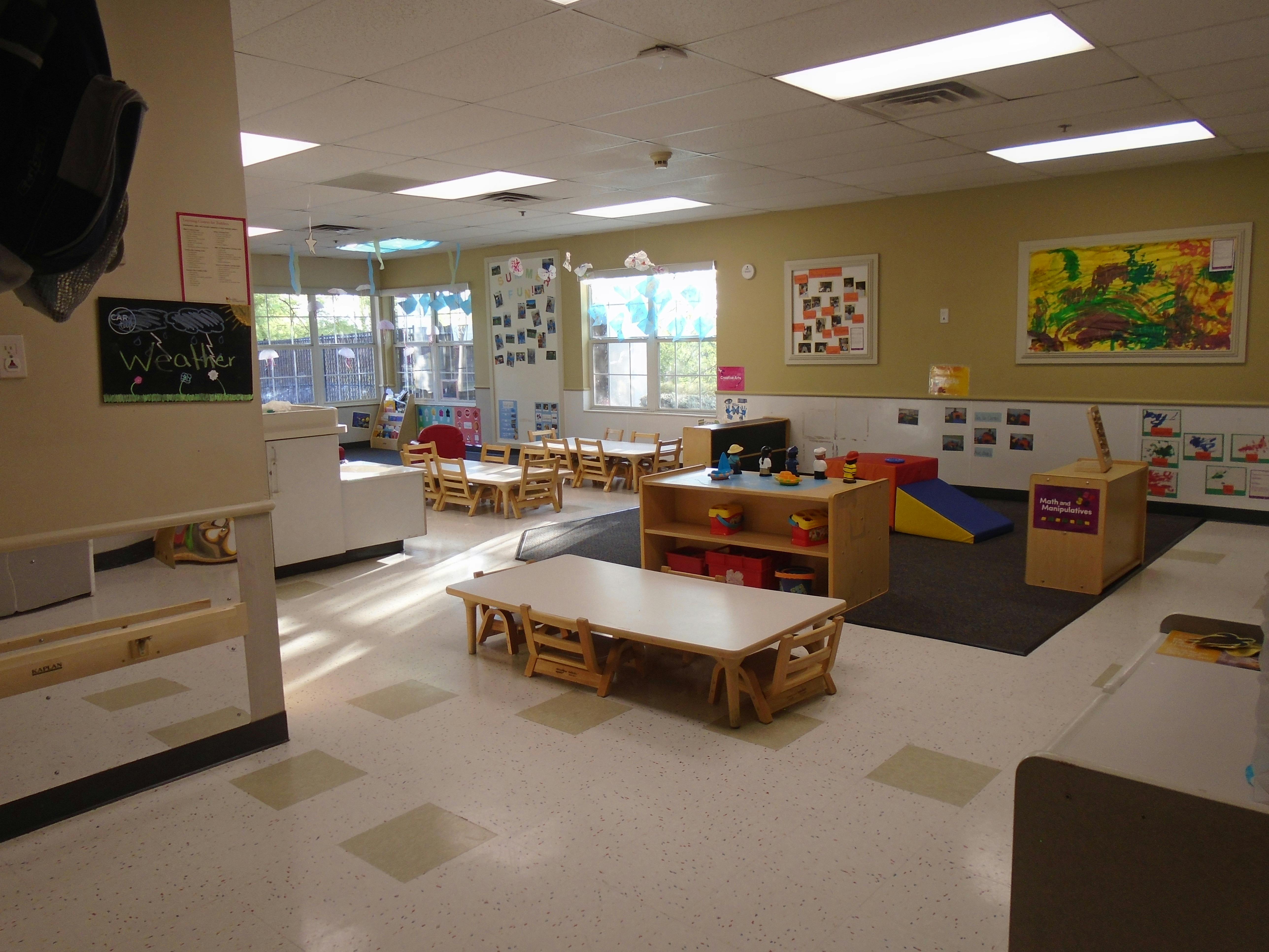 An empty early childhood classroom with small tables and chairs, and play areas