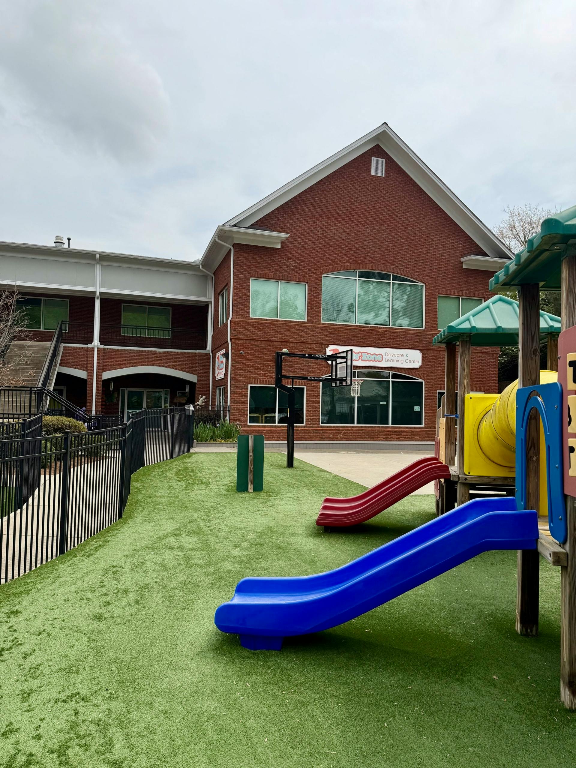 Playground with slides and a basketball hoop outside a brick building