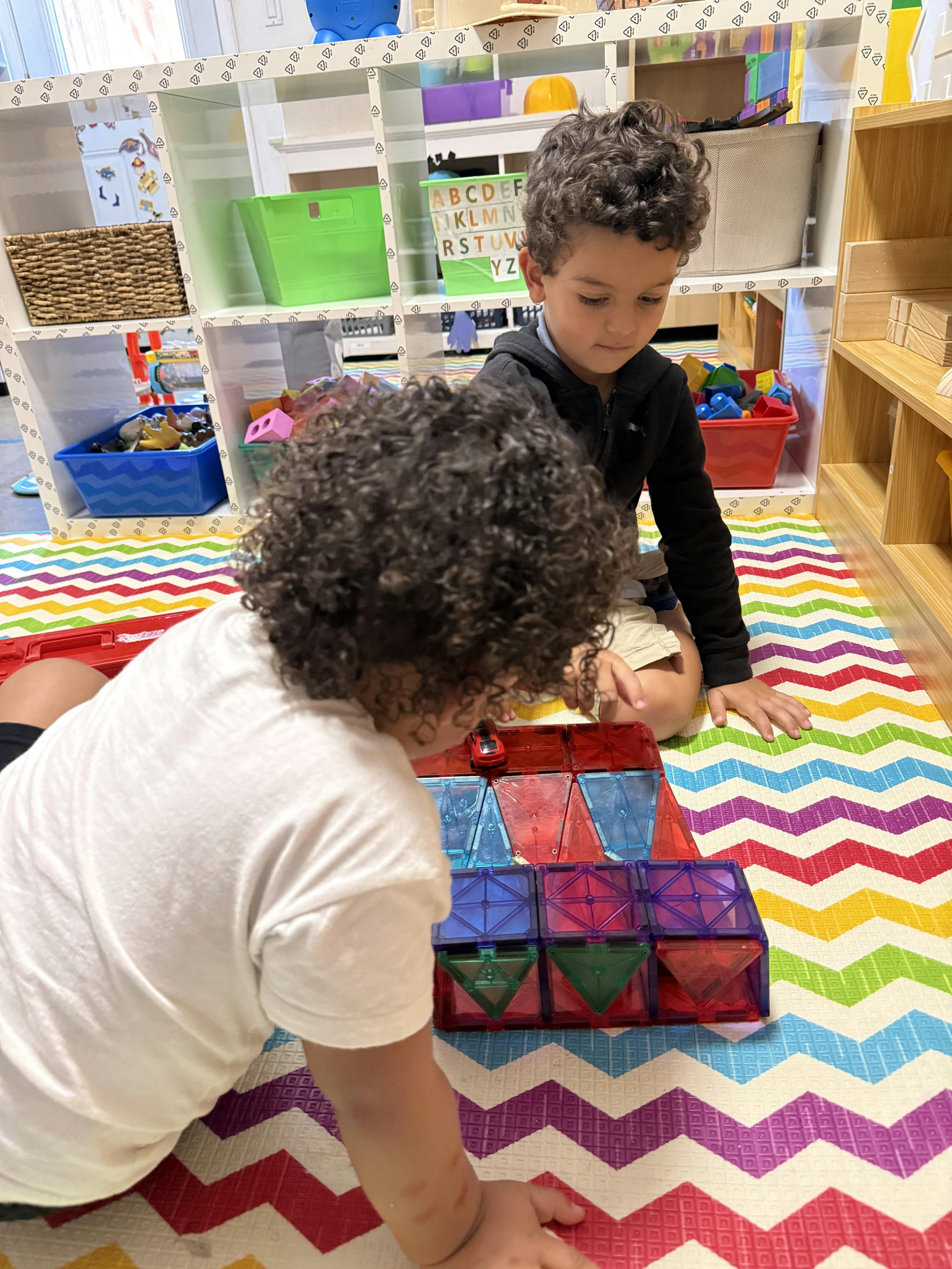 Two children playing with magnetic building tiles on a patterned rug