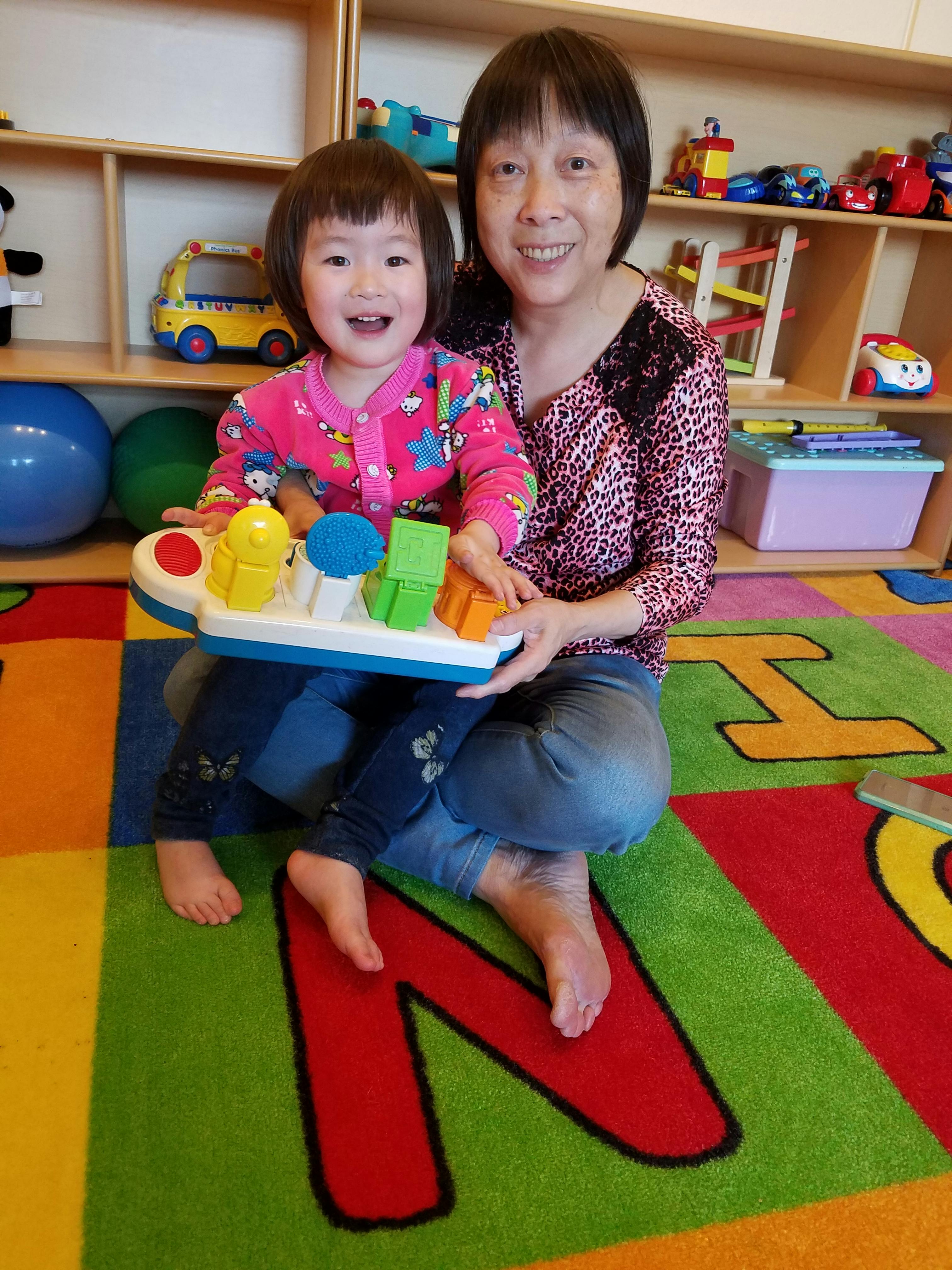 Person and child sitting on a colorful rug, holding a toy