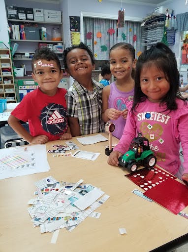 Four children standing around a table with papers and a toy tractor