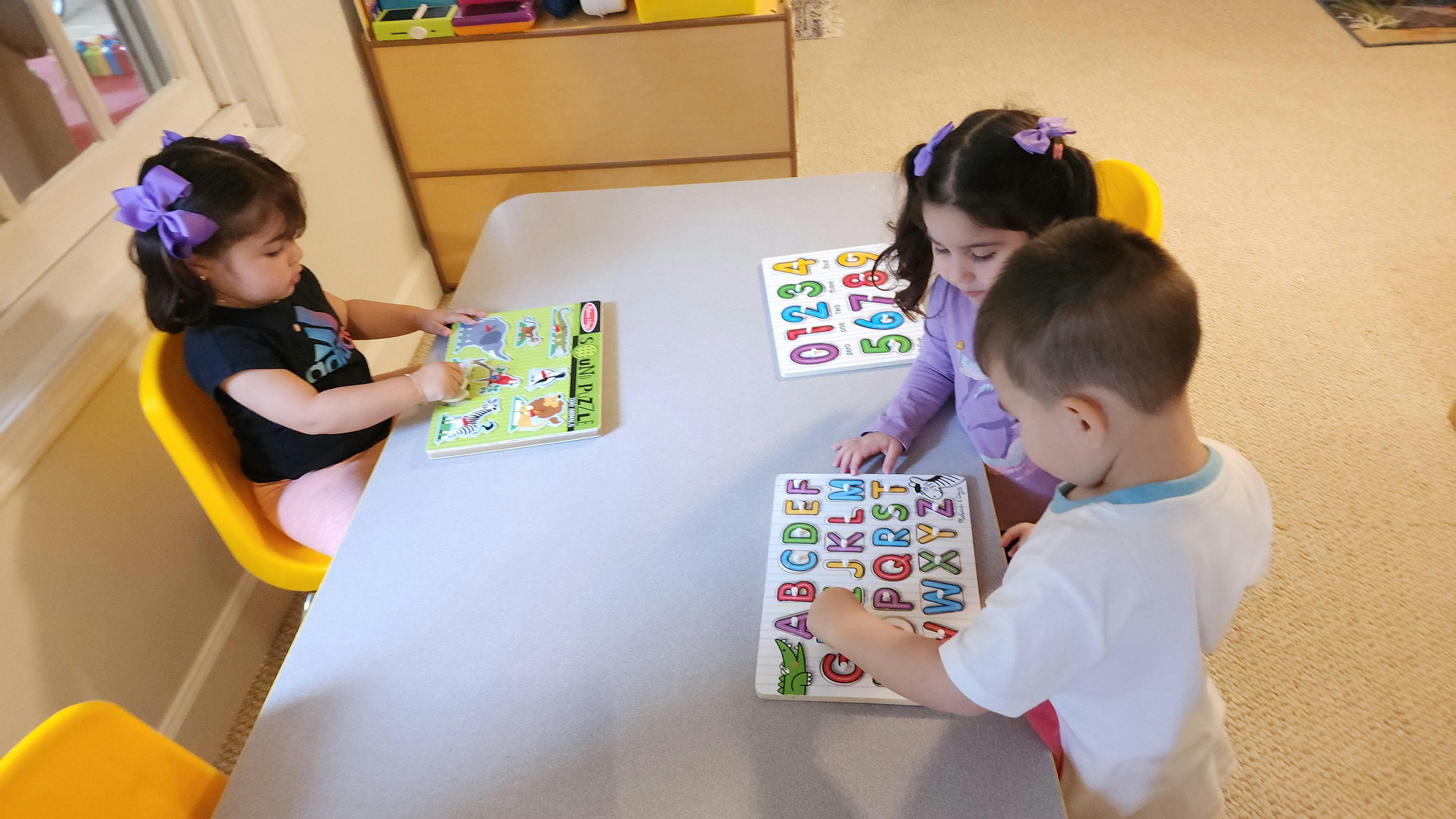 Three children at a table with alphabet puzzles and a book