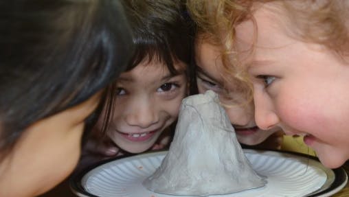 Three children looking at a small volcano model on a paper plate
