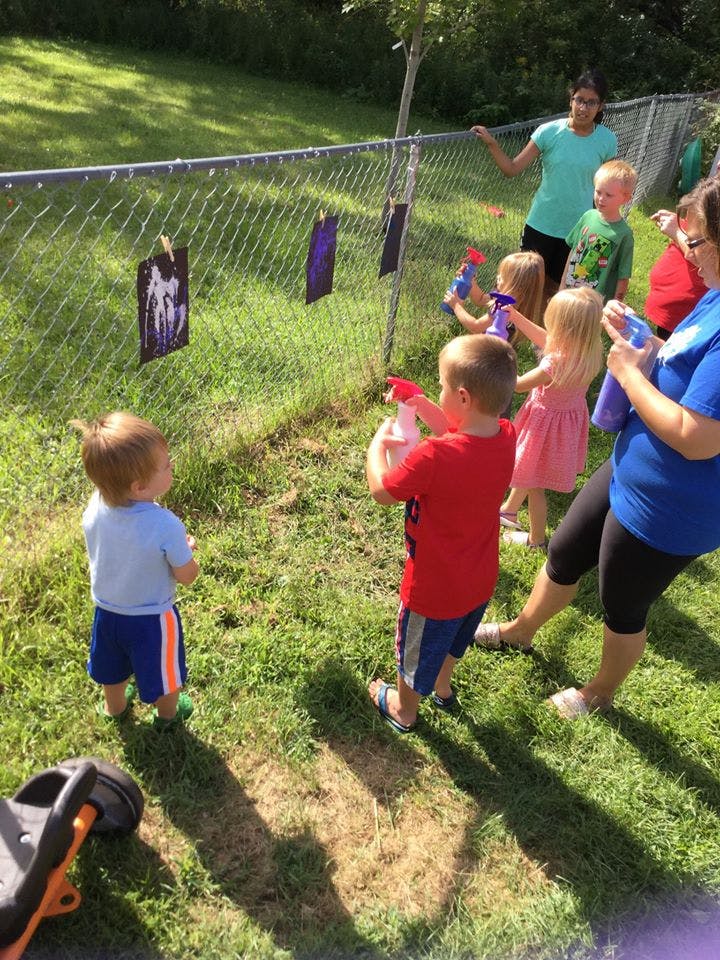 Children and adults spraying water bottles at targets on a fence