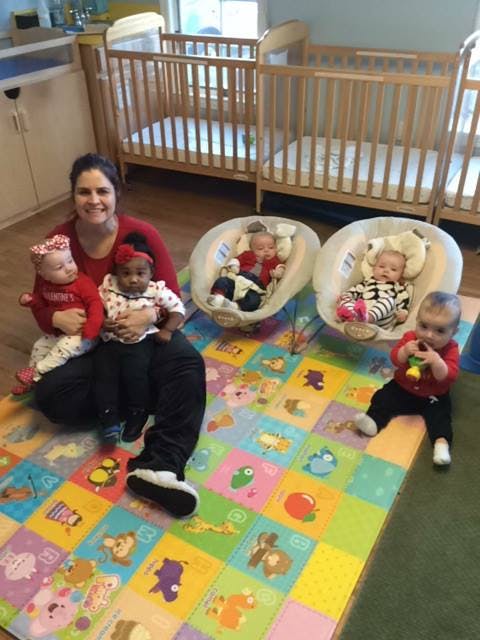 Person sitting on floor holding two children, with three other children nearby