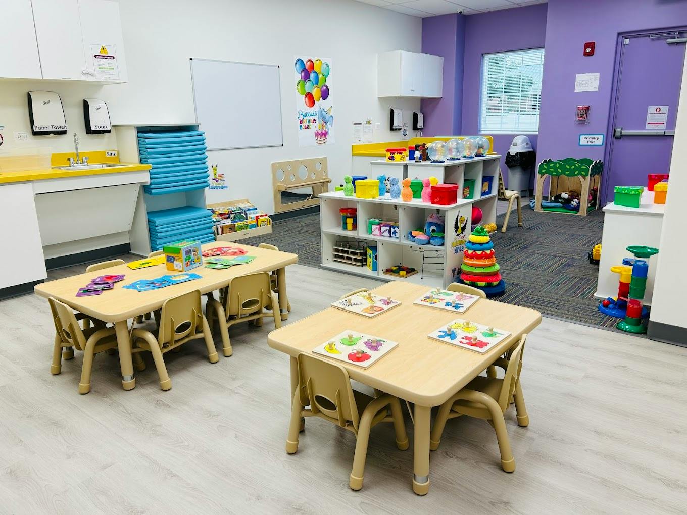 Empty classroom with small tables and chairs, shelves with toys