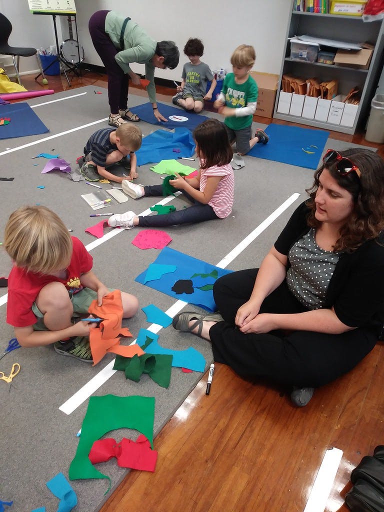 Adults and children sitting on the floor cutting and arranging colorful paper