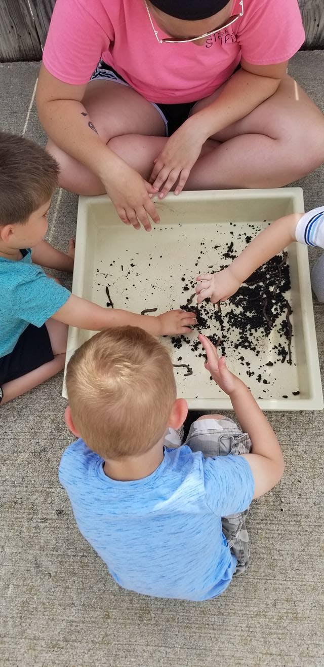 Person and children playing with dirt and worms in a tray