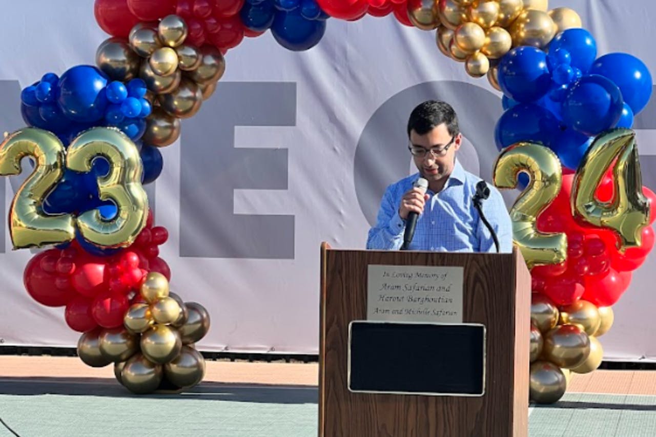Person speaking at a podium with a microphone under a balloon arch