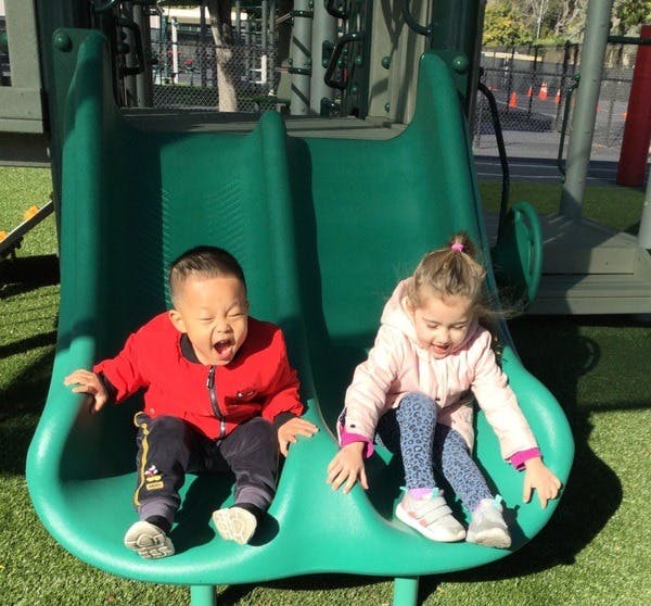 Two children sitting on a green playground slide