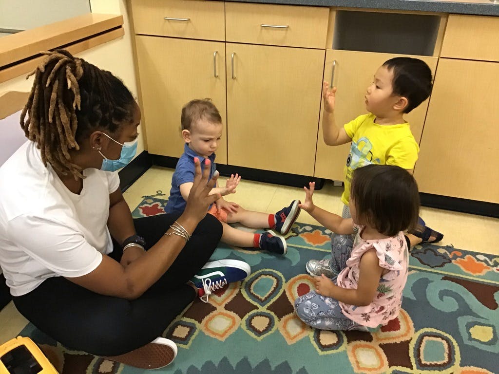 Person and three children sitting on a rug, raising hands