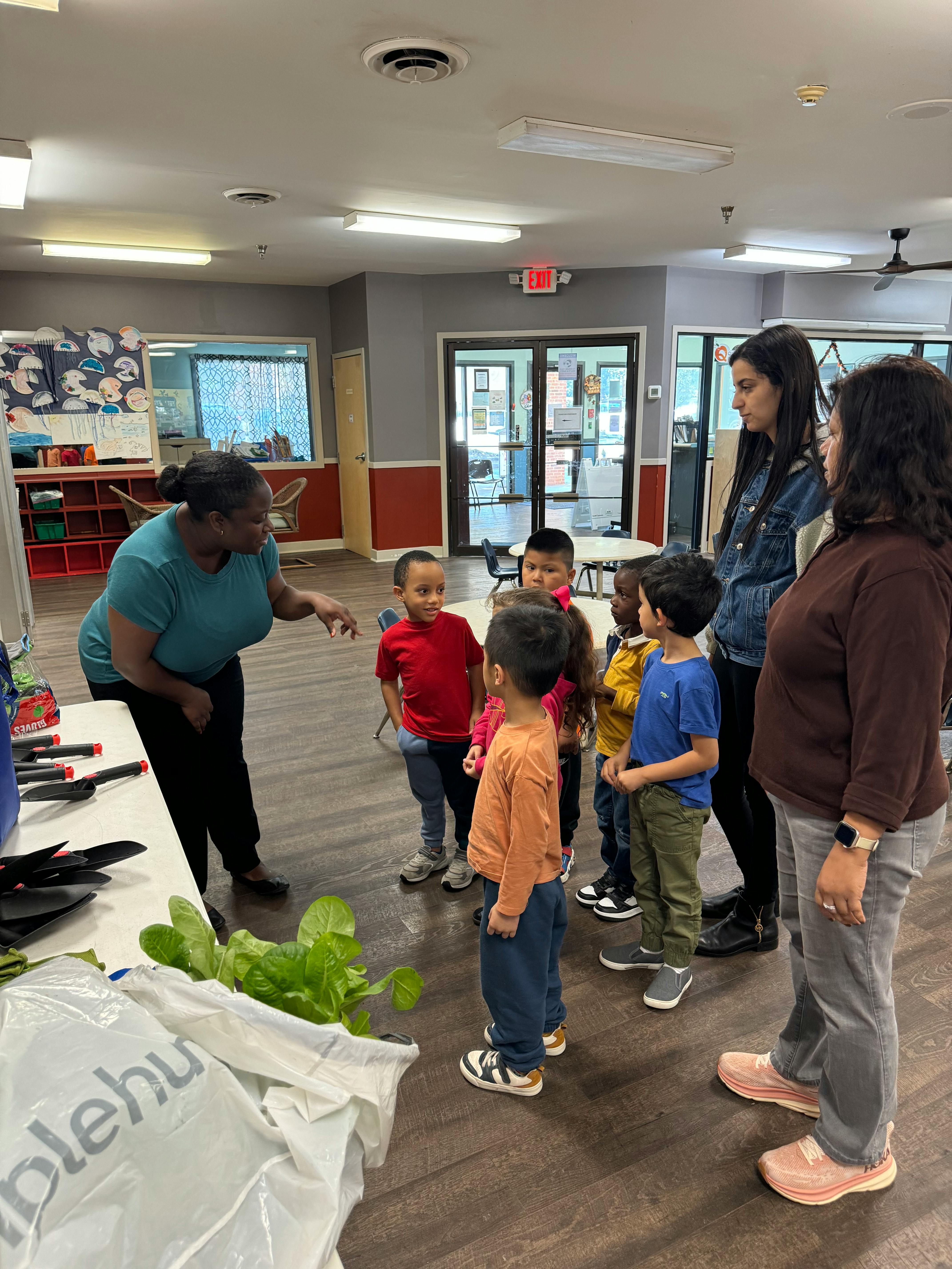 Adult speaking to a group of children and two adults in a room