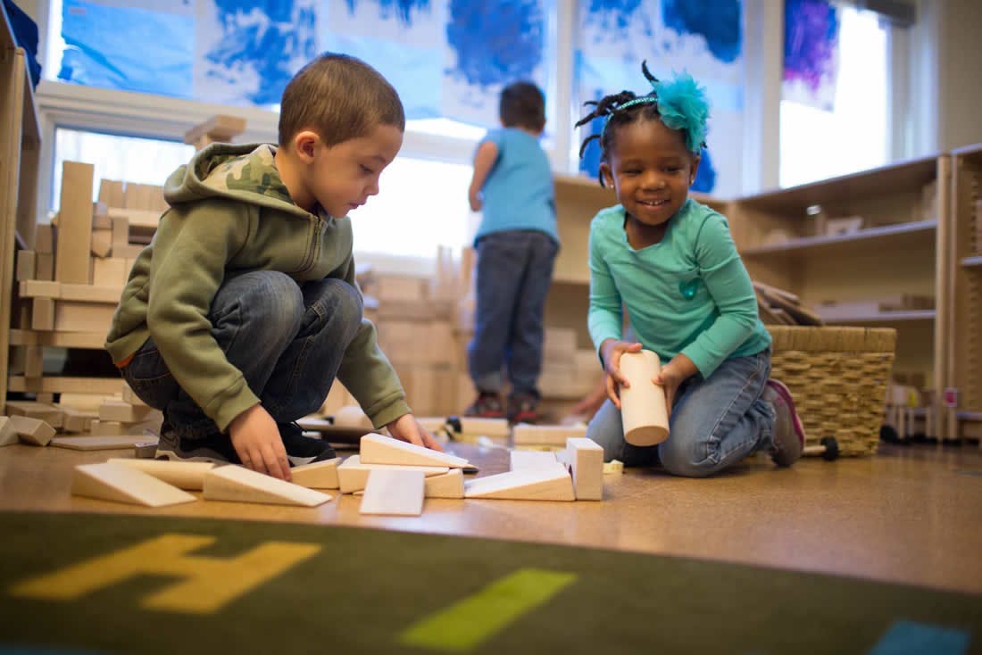 Two children playing with wooden blocks on the floor