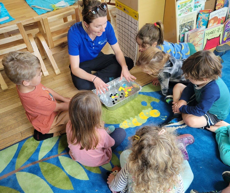 Adult and children sitting on a rug, looking at items in a tray