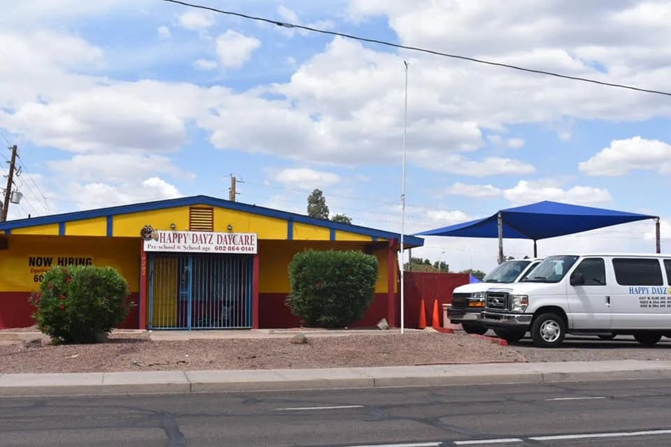 Yellow and red building with "HAPPY DAYZ DAY CARE" sign and two white vans