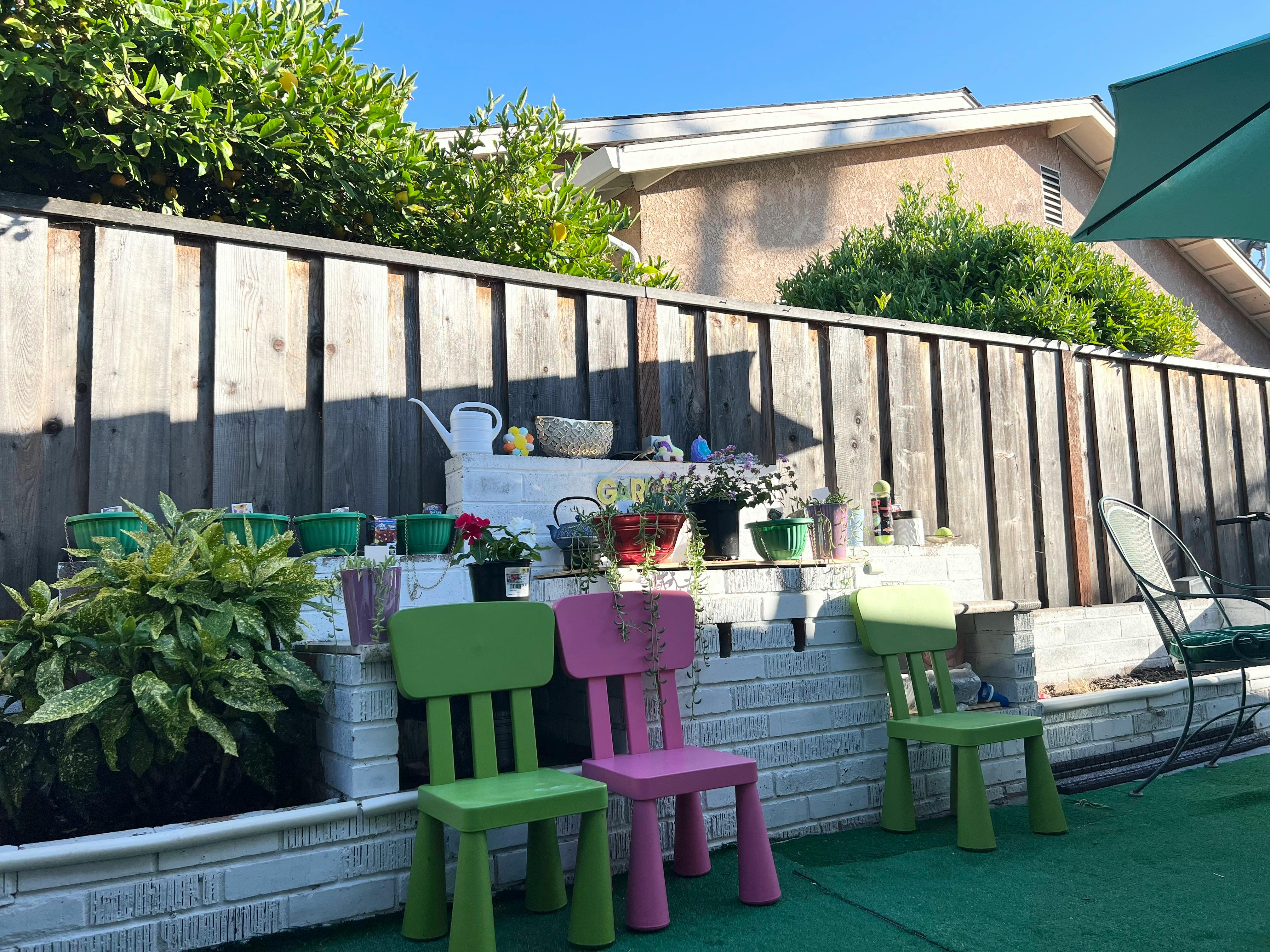 Three small chairs in front of a wooden fence with plants and pots