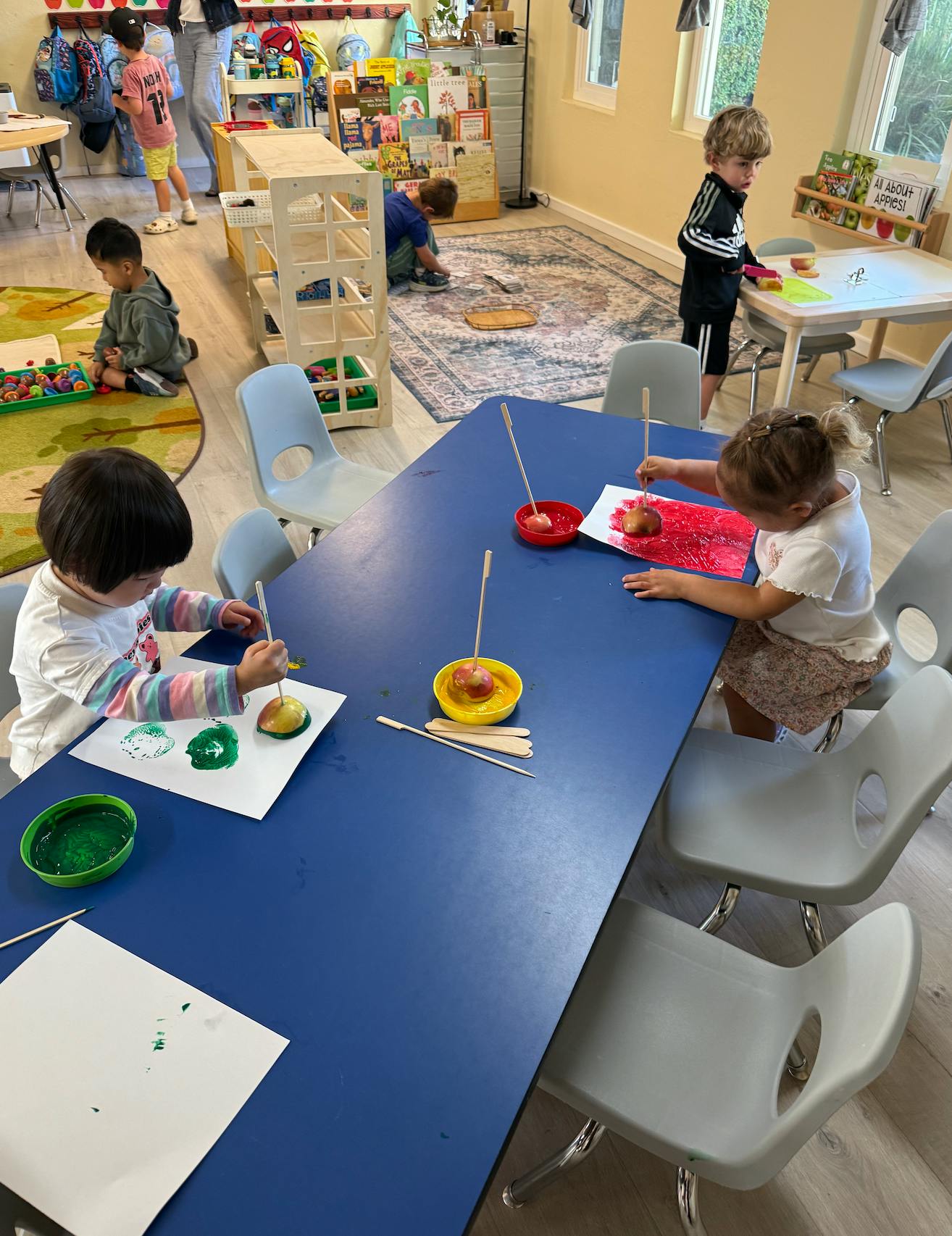 Children painting on paper using apple halves as stamps in a classroom