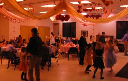 People gathered in a decorated room, some seated at tables, others standing and dancing