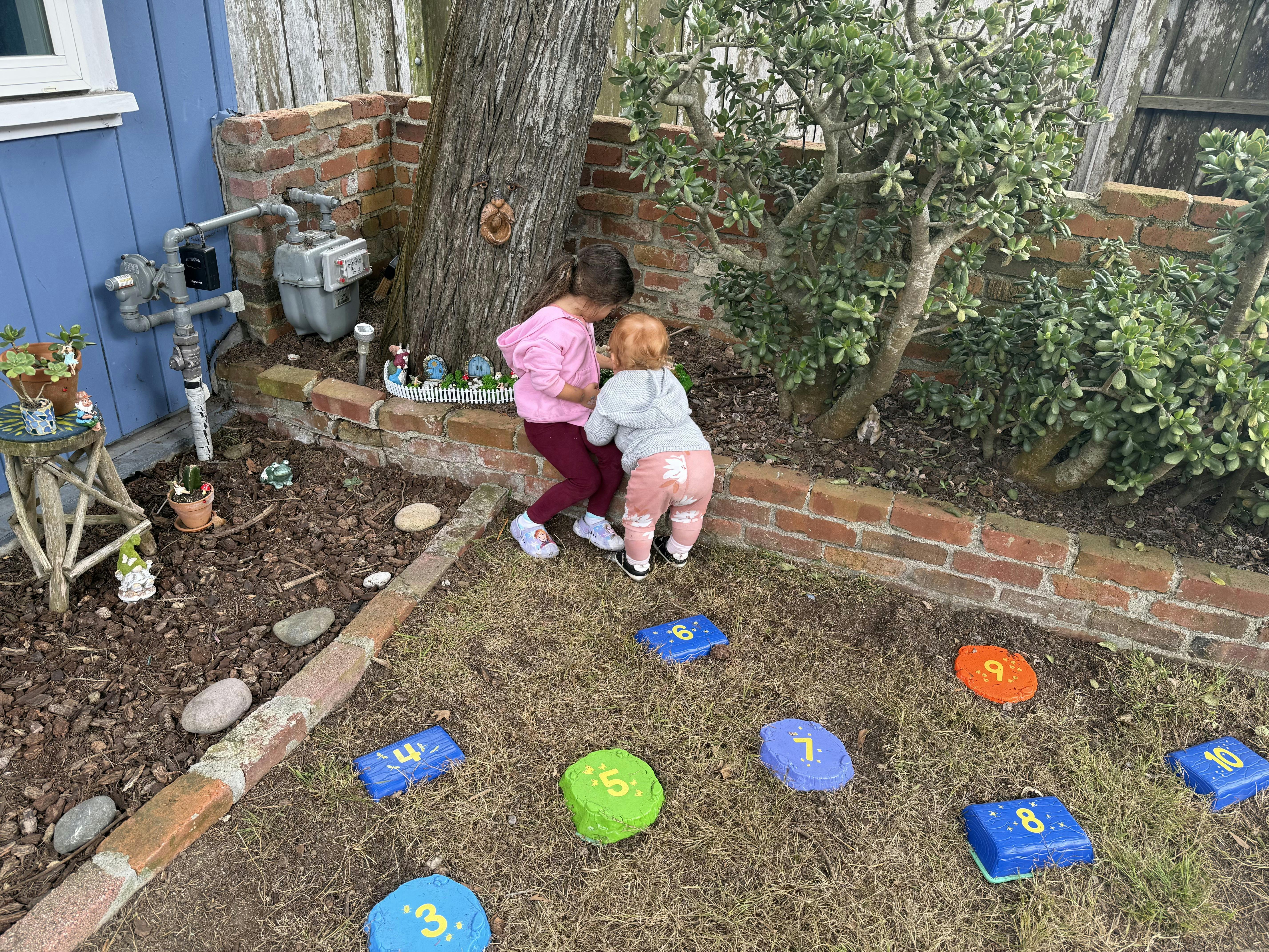 Two children playing near a tree and brick wall in a yard