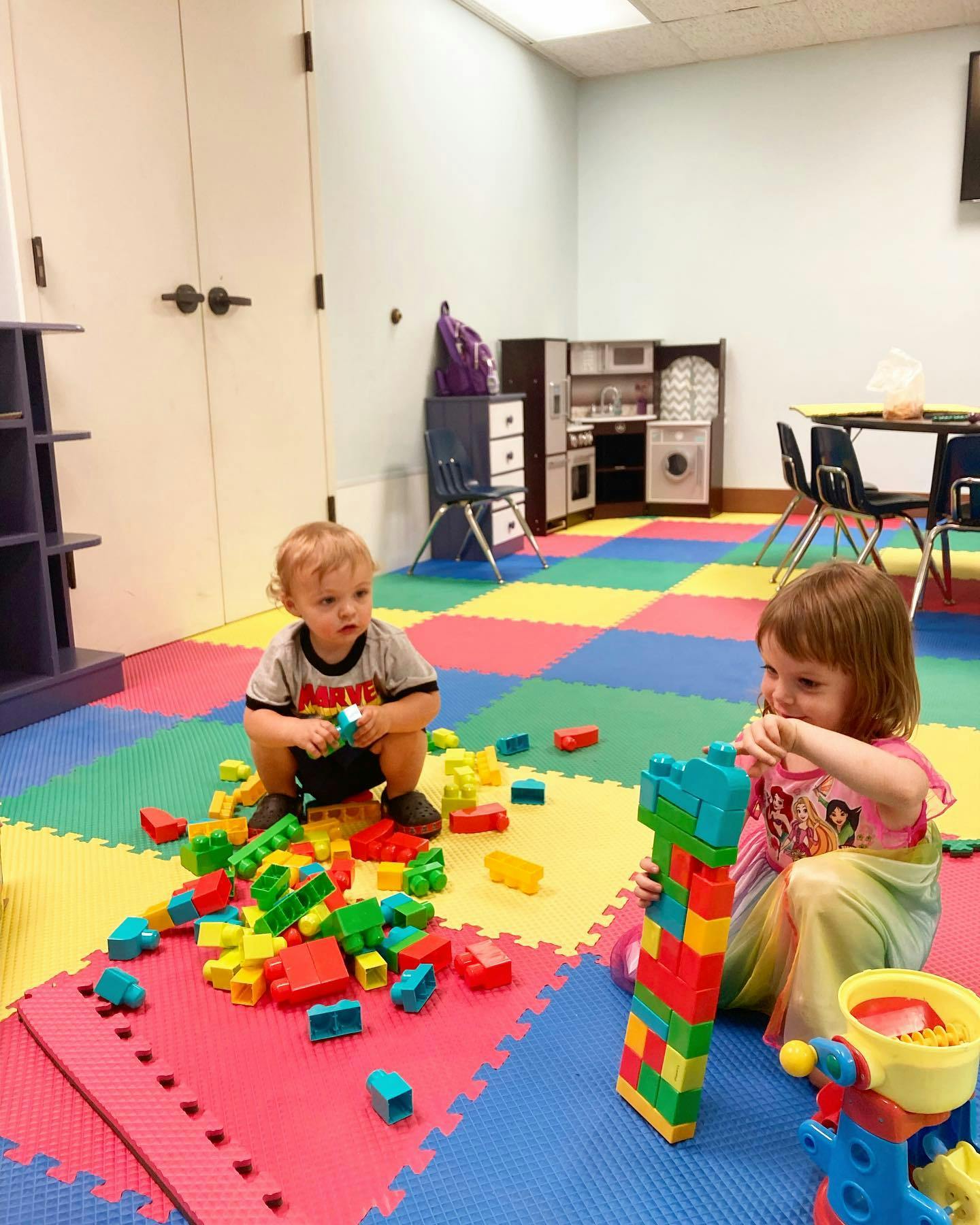 Two children playing with colorful building blocks on a patterned floor
