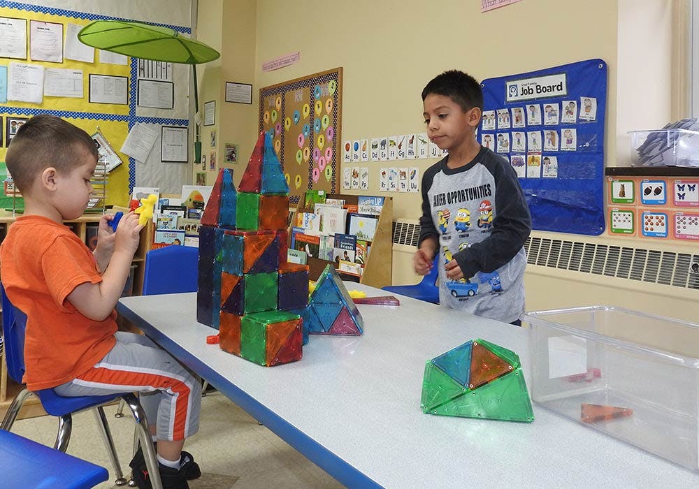 Two children playing with magnetic building blocks at a table in a classroom