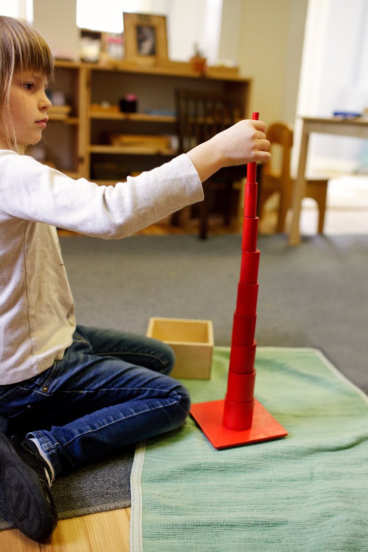 Child sitting on floor holding a red stacking toy