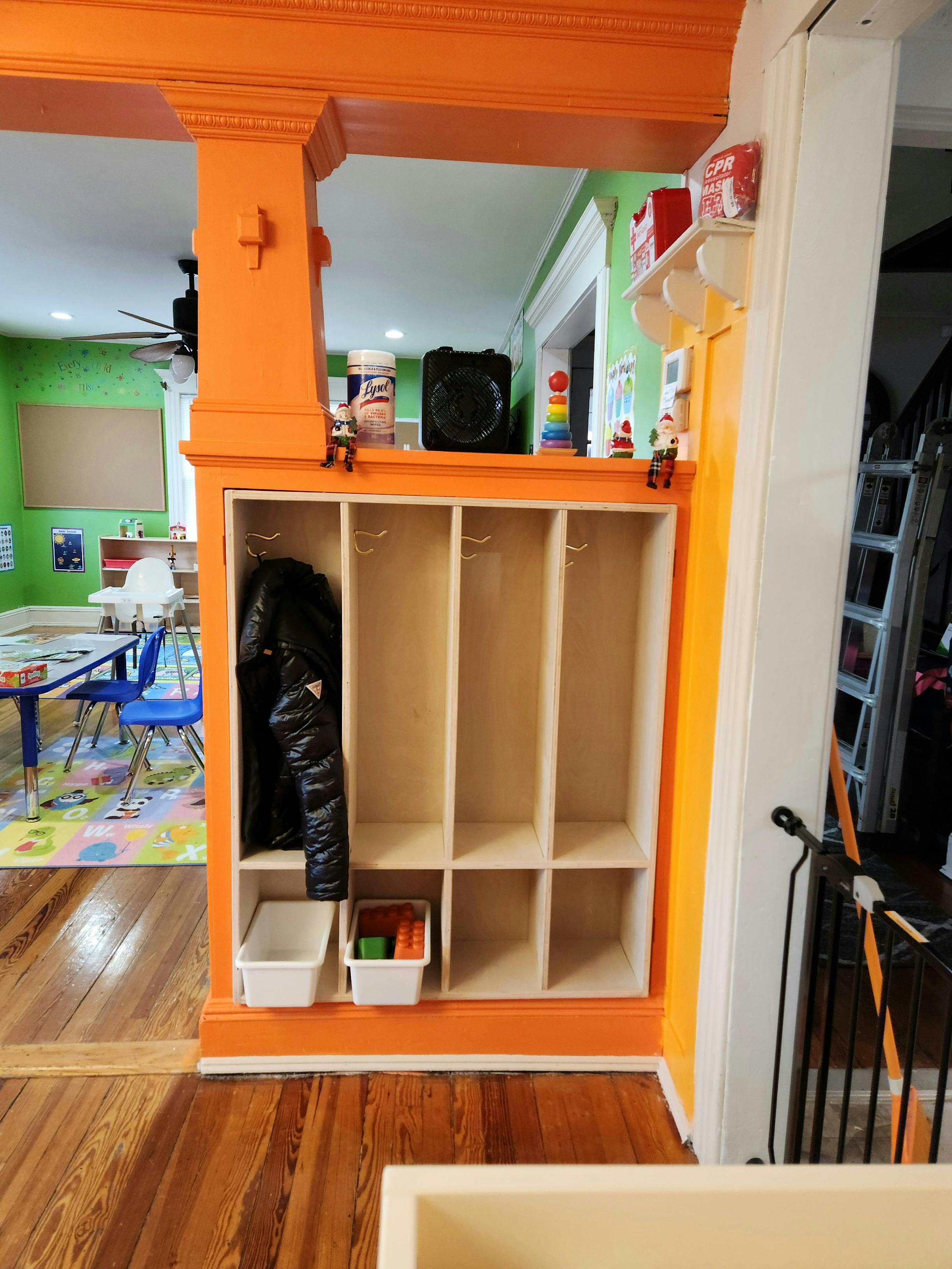Orange cubby storage unit with a black jacket and bins, in the background, a classroom