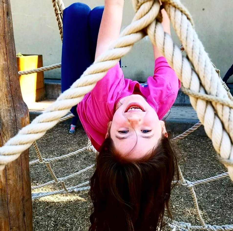 Child hanging upside down from ropes on a playground