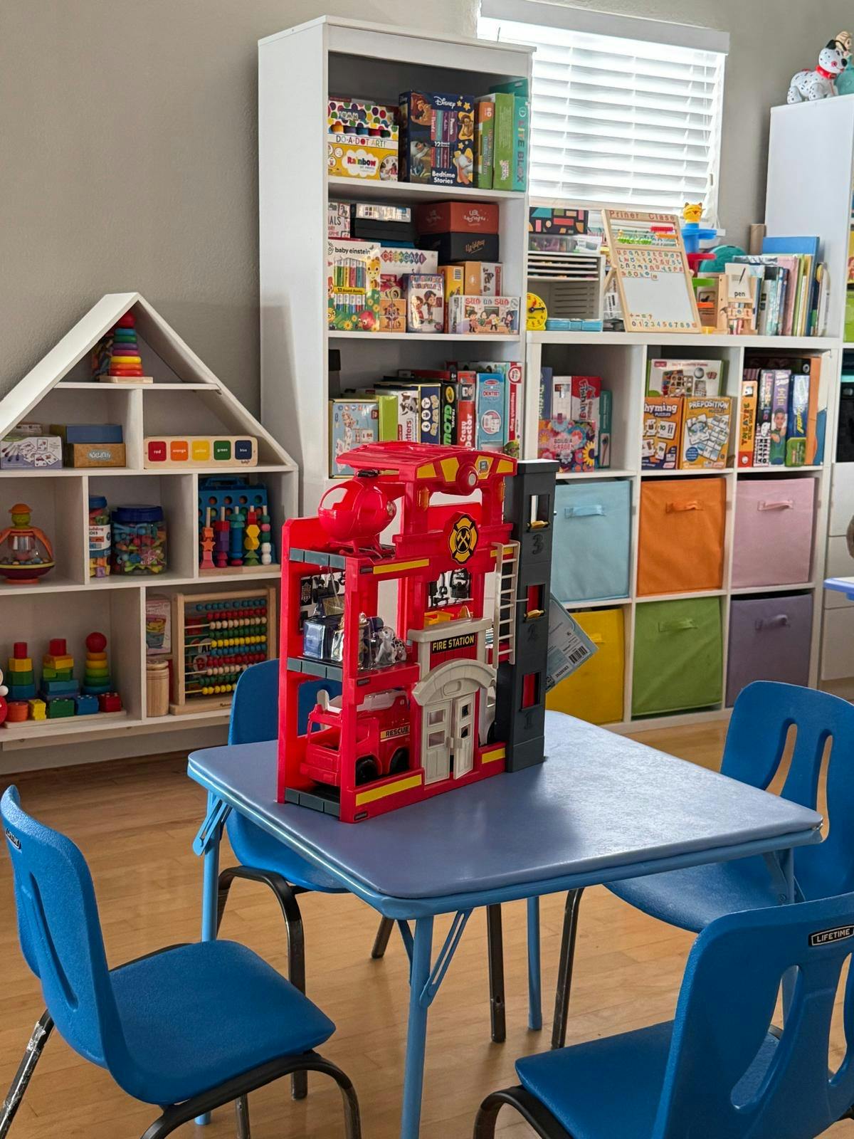 Playroom with a blue table and chairs, a red toy fire station, and shelves of toys