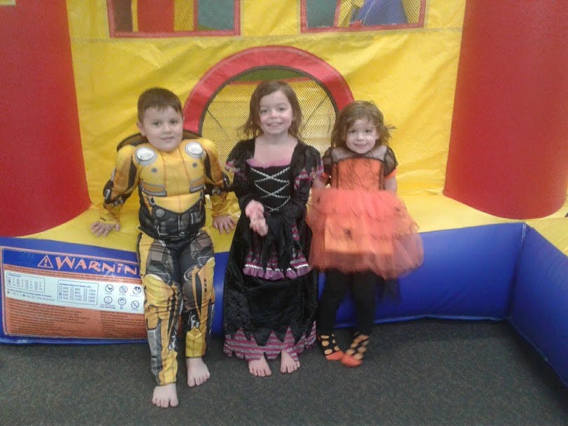 Three children in costumes standing in front of an inflatable bounce house