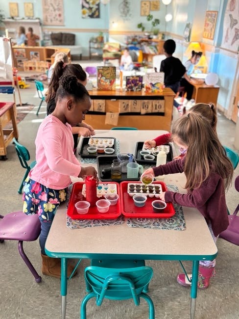 Children at a table in a classroom, pouring liquids into containers