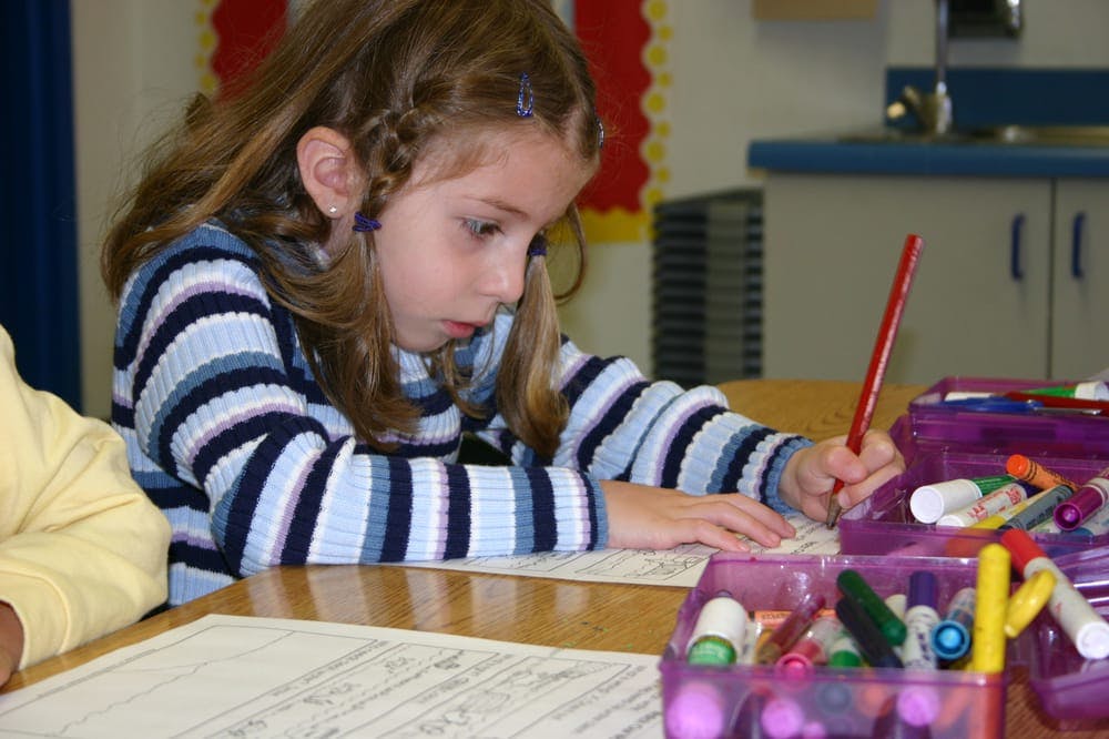 Child drawing with a red pencil at a table