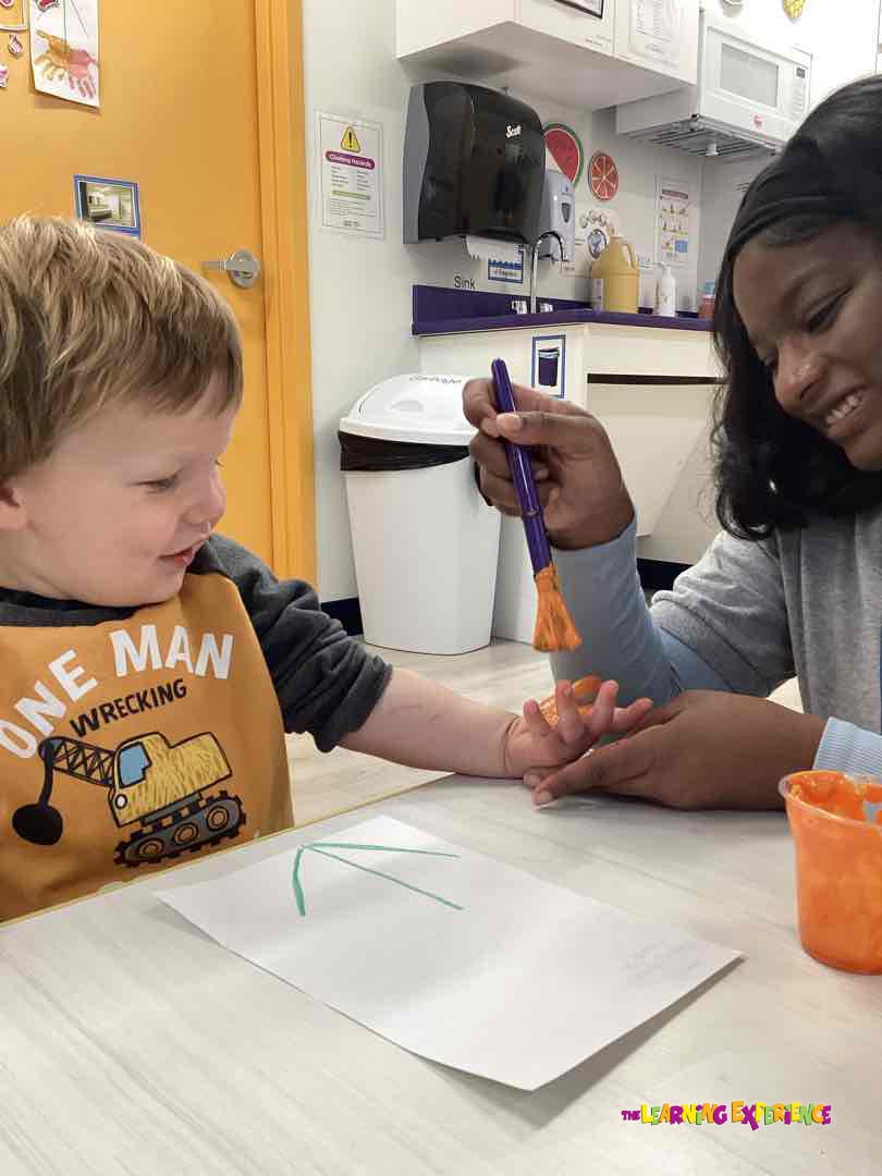 Person painting a child's hand with orange paint