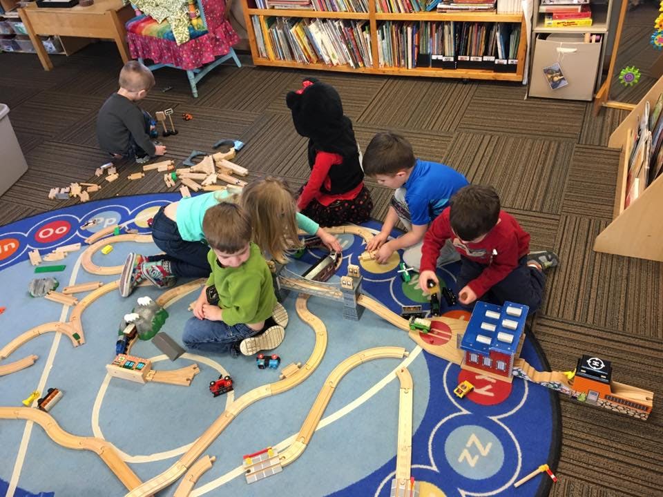 Children playing with a wooden train set on a rug