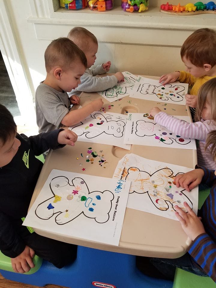 Children decorating teddy bear cutouts with small colorful pieces