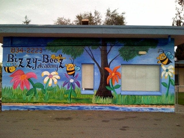 Mural on a building with flowers, bees, a tree, and "Bizzy-Bee Academy"