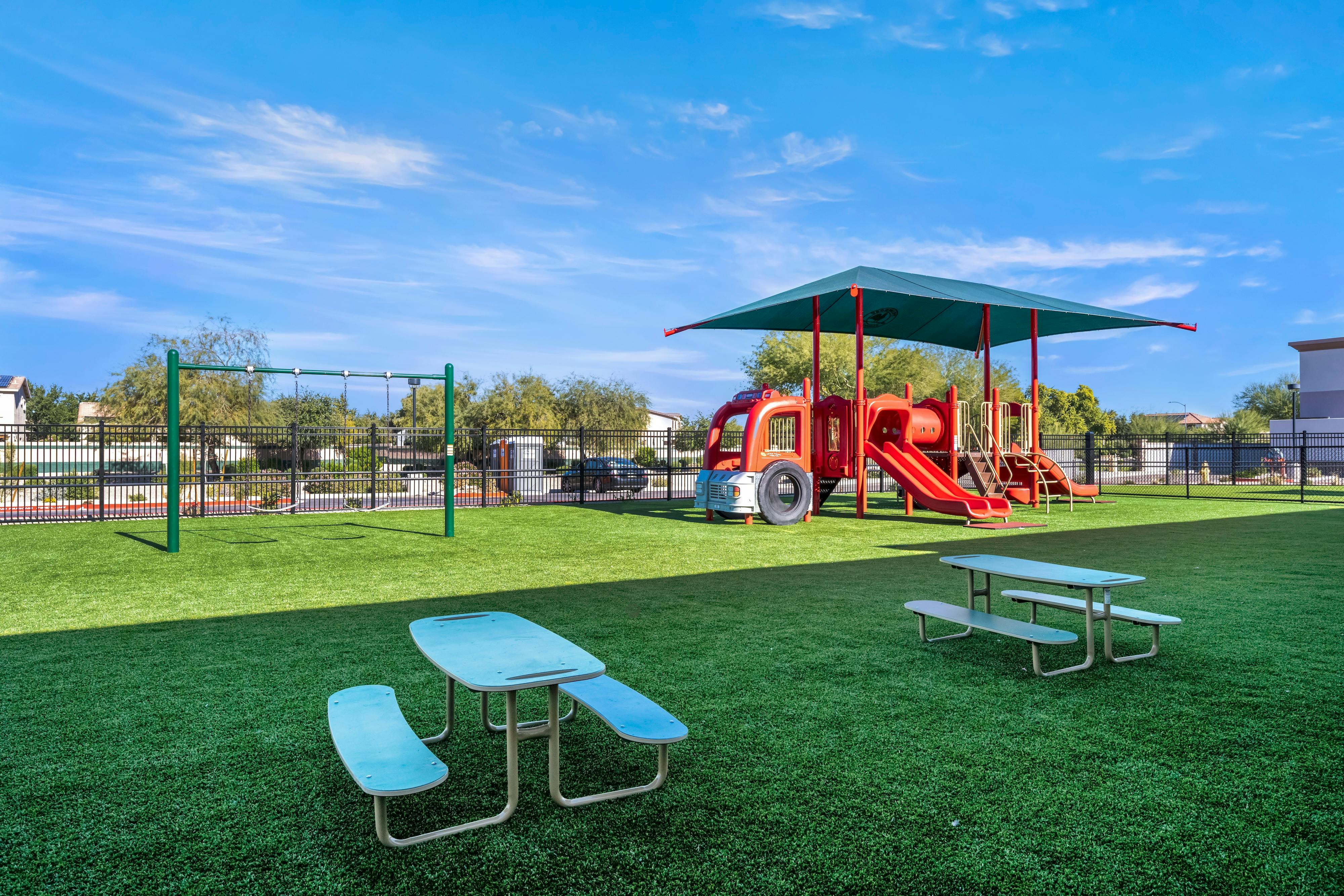 Playground with fire truck climbing structure, swings, and picnic tables on artificial grass