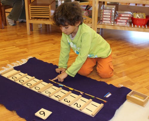 Child kneeling on floor, pointing at a wooden number board