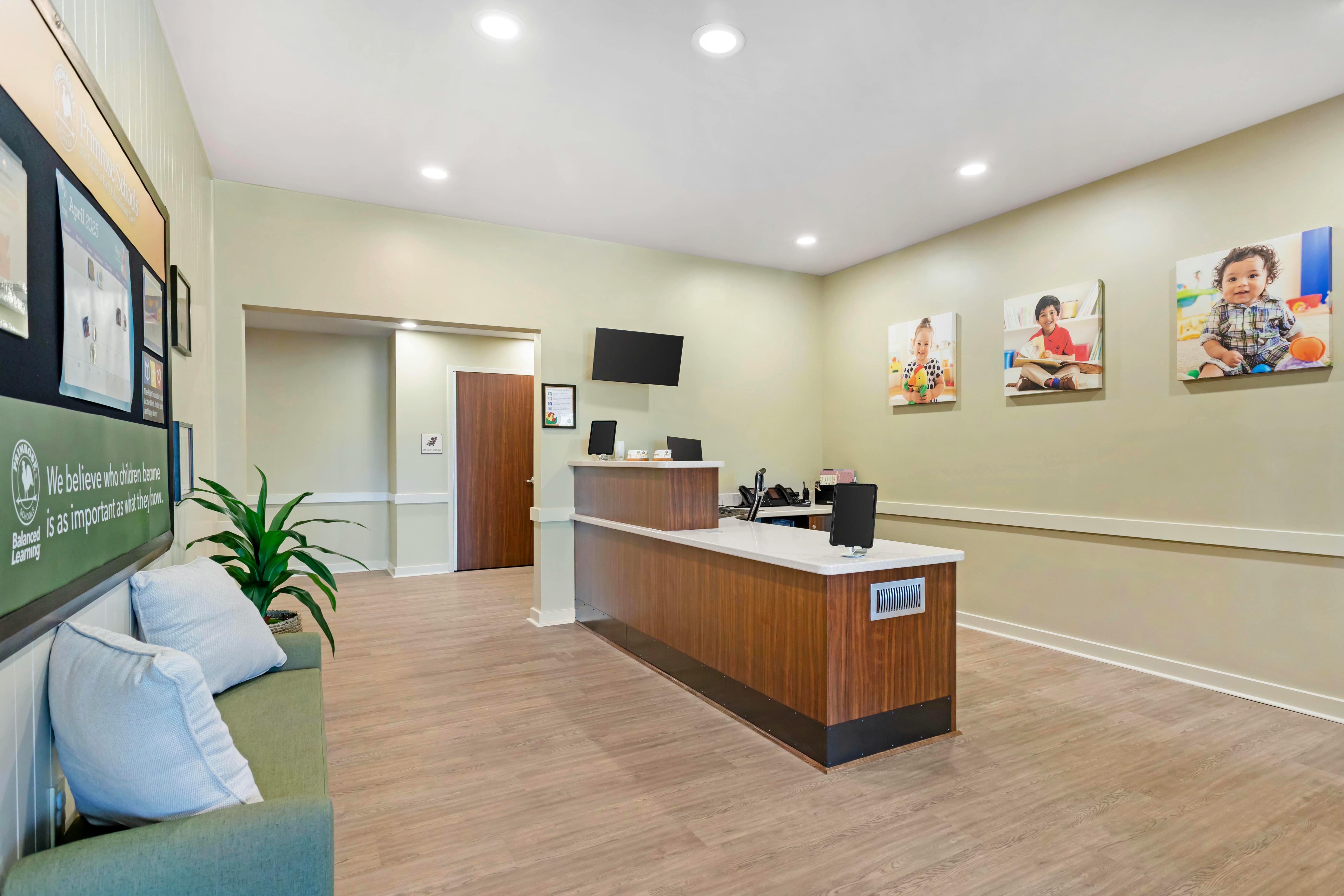 Reception area with a wooden desk, a green couch, and pictures of children on the wall