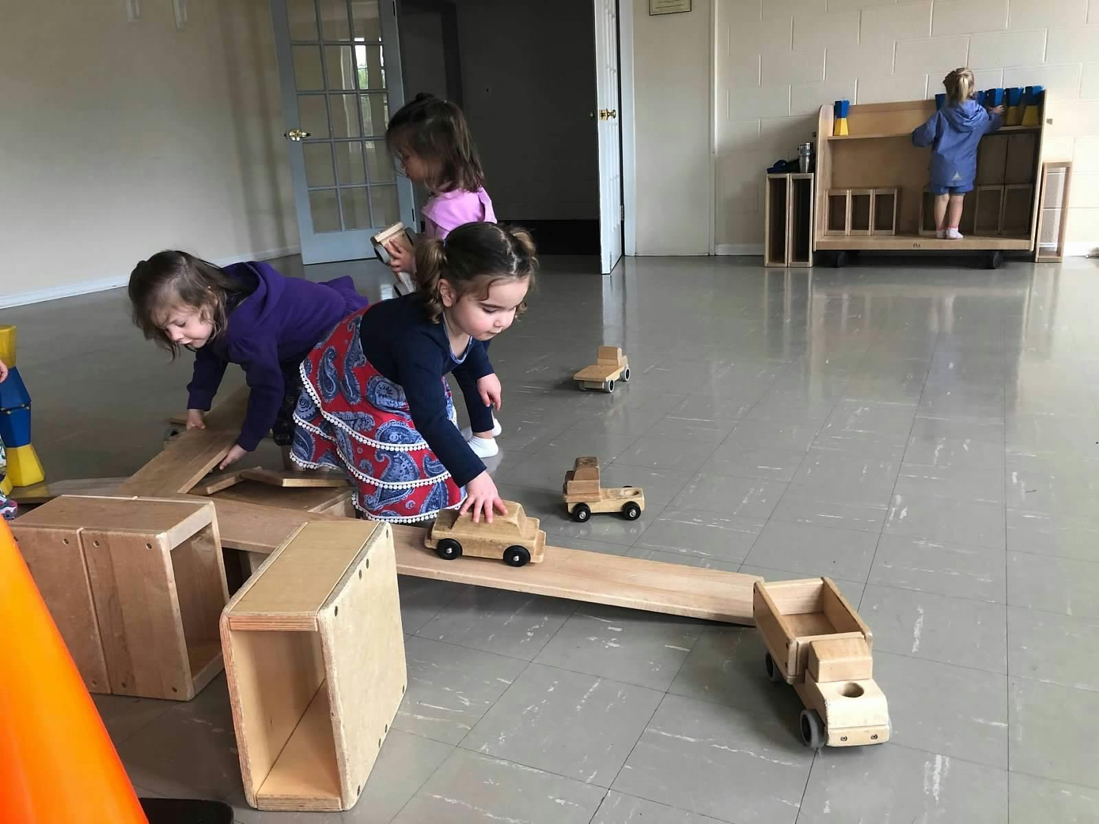 Children playing with wooden blocks and toy trucks on the floor