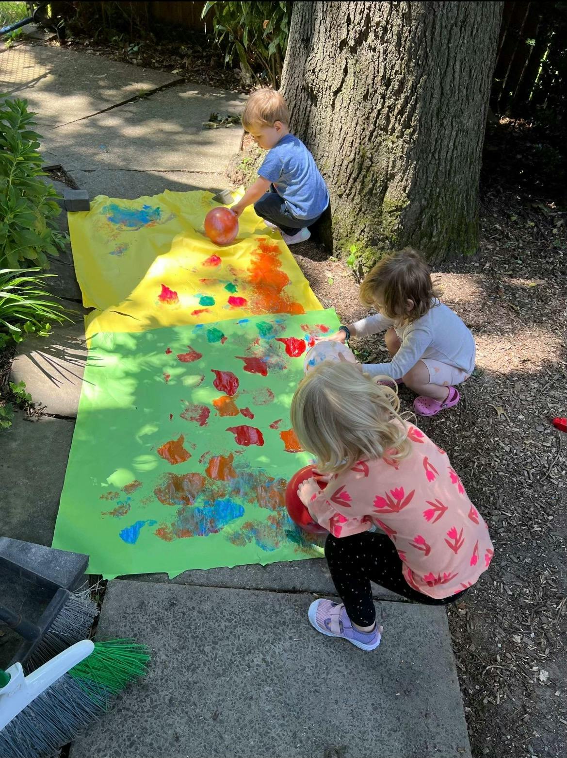 Three children painting on a long sheet of paper outdoors