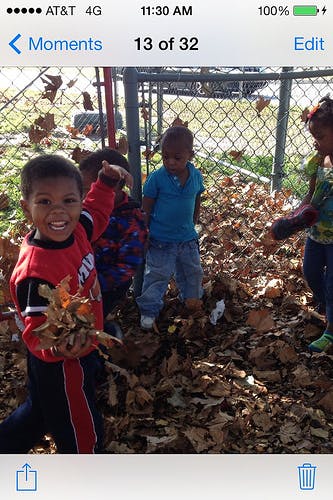 Child holding a pile of leaves with other children in a leaf-covered area