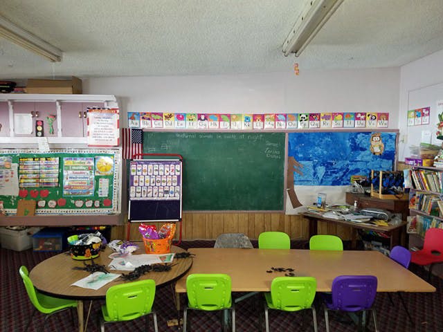 Classroom with tables and chairs, chalkboard, and bulletin boards