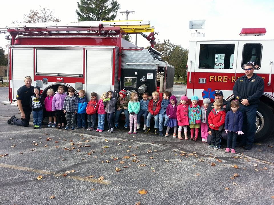 Two people with a group of children in front of two fire trucks