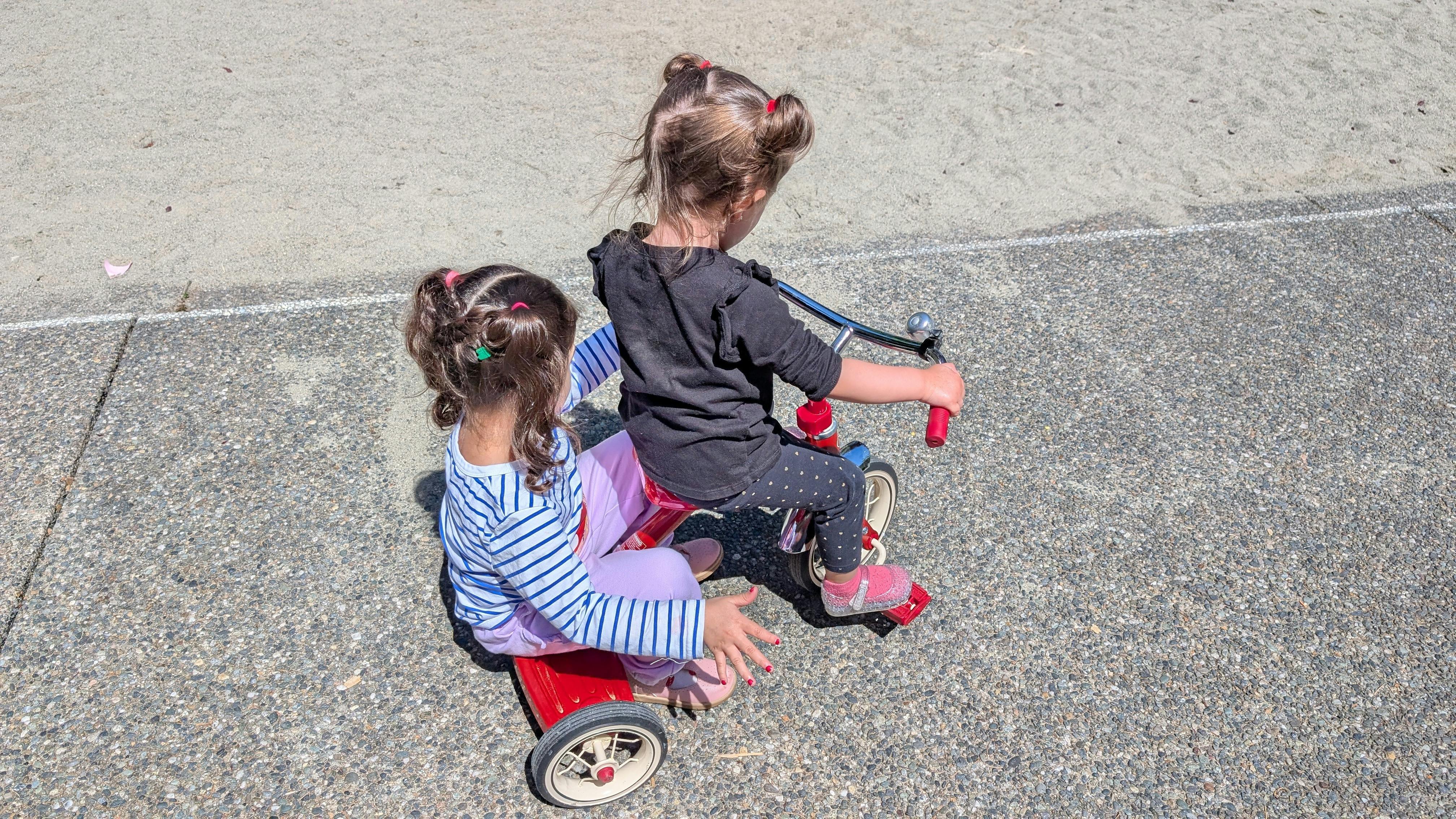 Two children on a red tricycle on asphalt