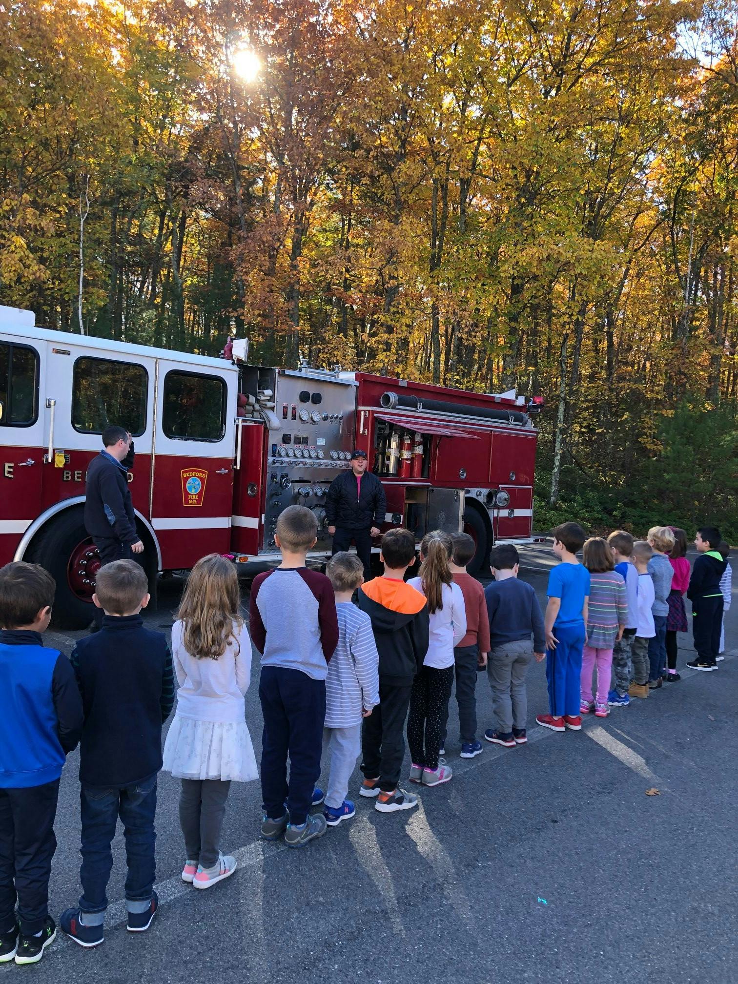 Children in a line watching adults near a fire truck