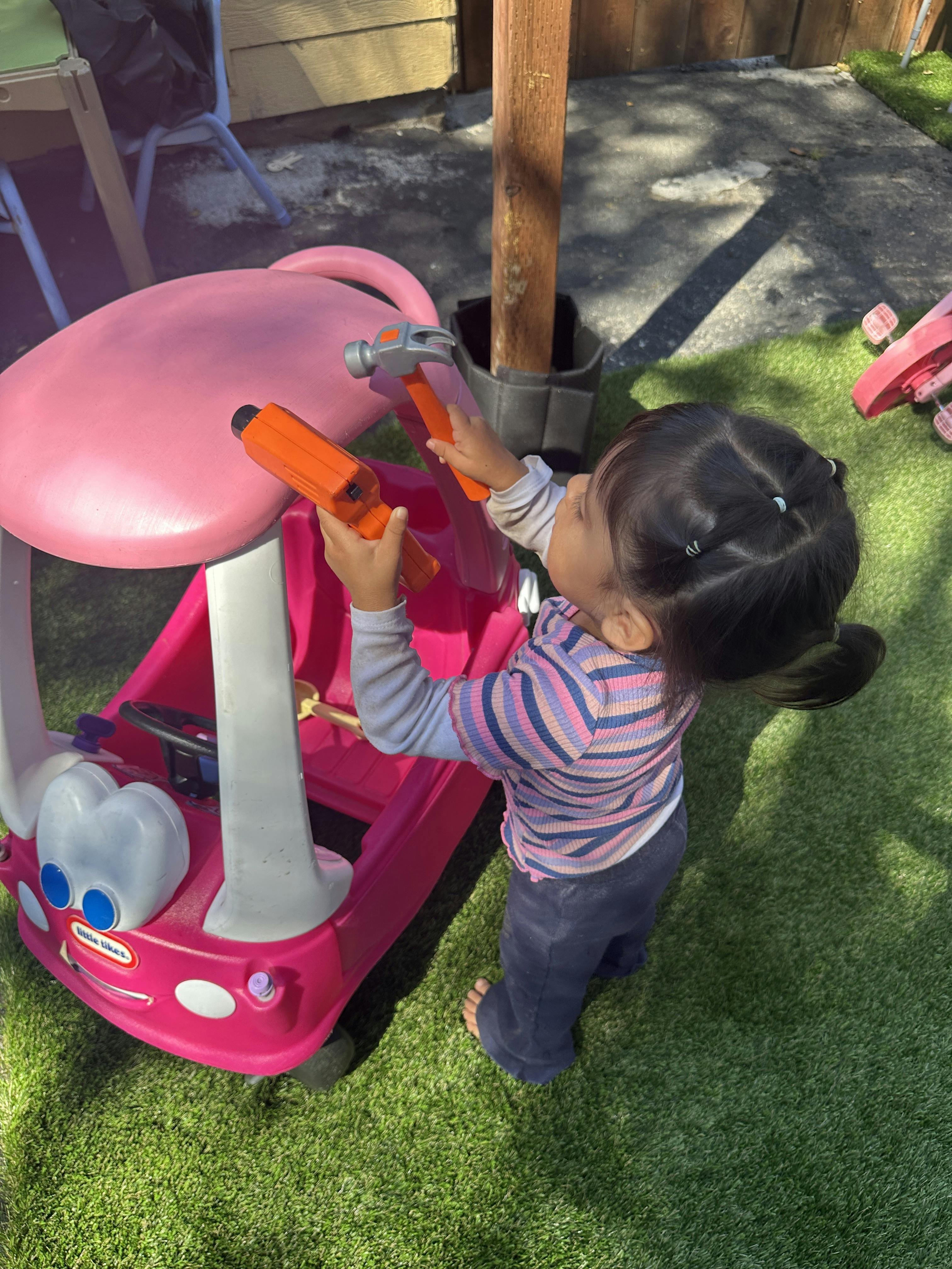 Child playing with toy tools next to a pink toy car