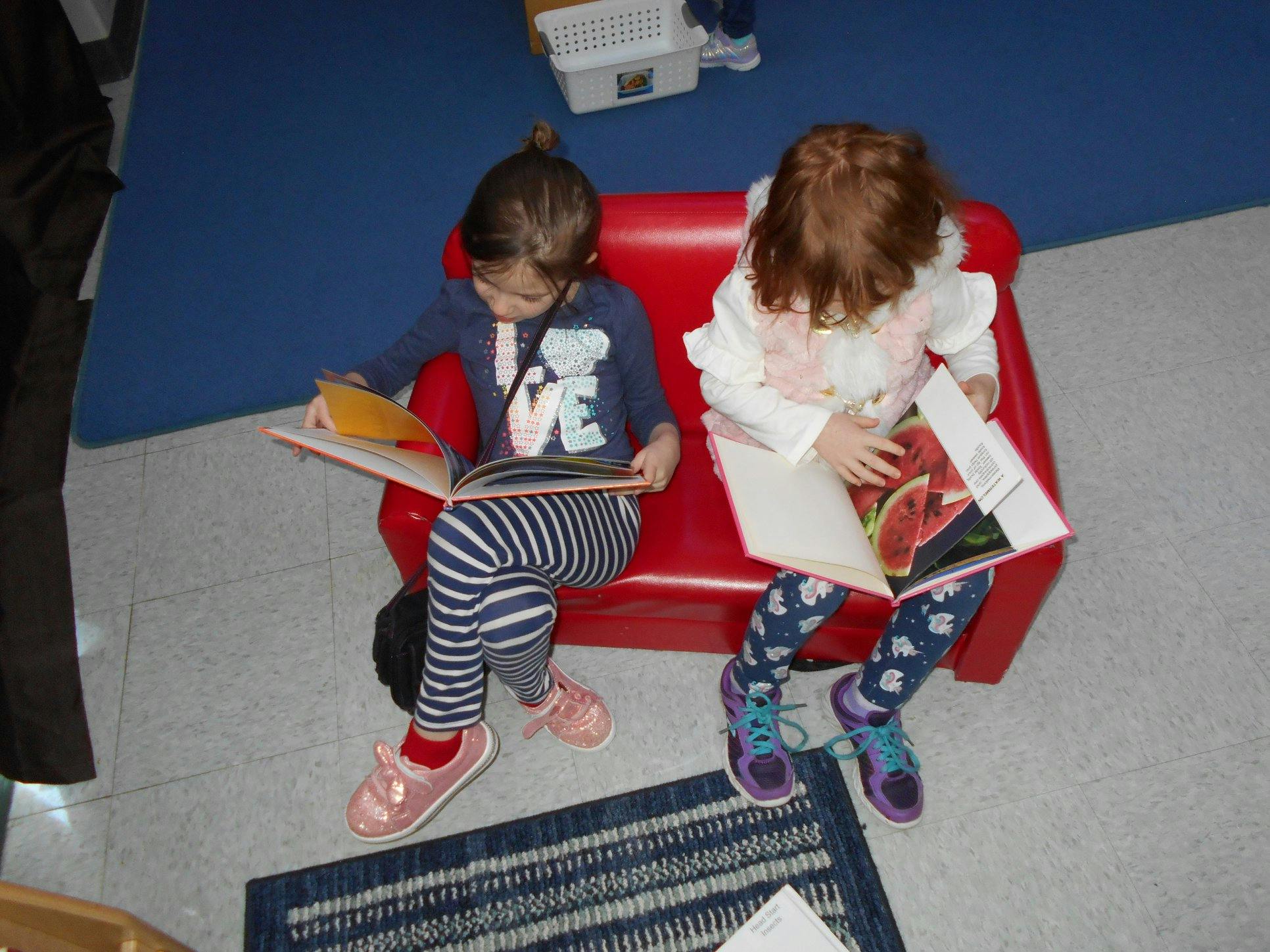 Two children sitting on a red couch reading books