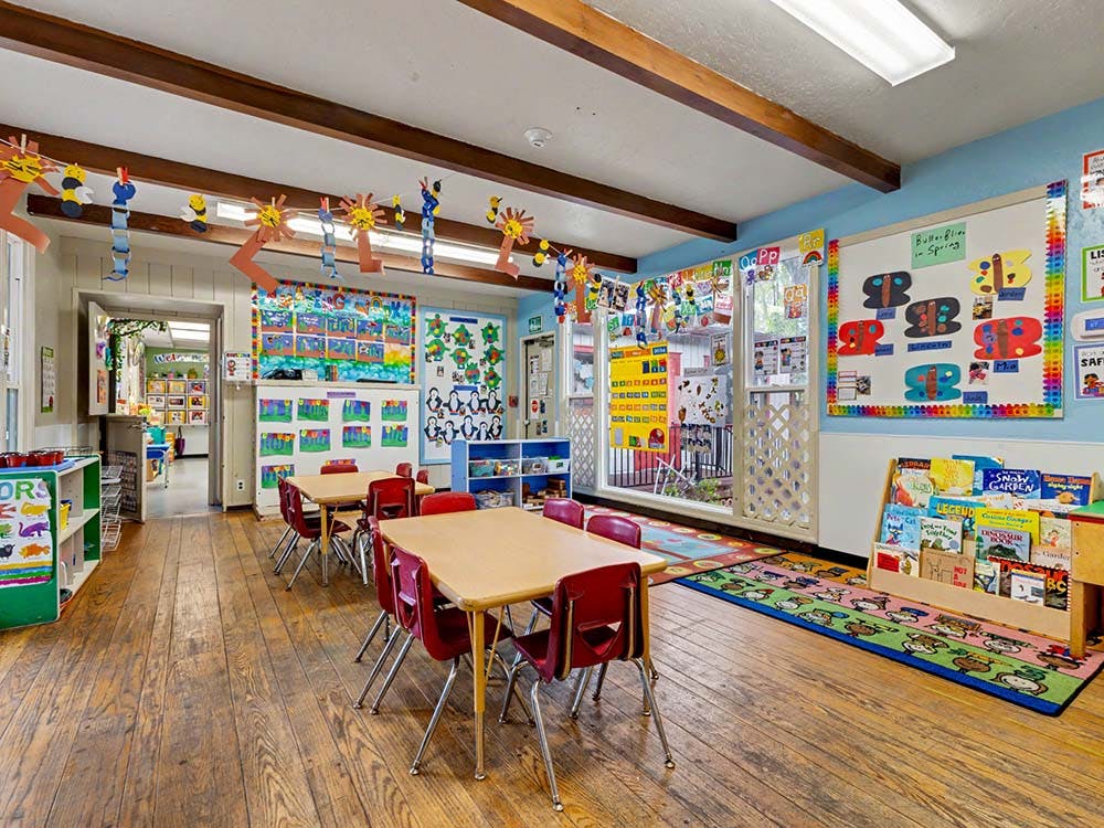 Classroom with small wooden tables and red chairs, colorful decorations